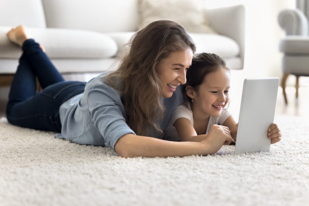 mom and daughter laying on carpet with tablet